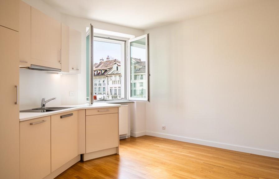 Helle Zürcher Wohnung mit geöffnetem Fenster, gepflegten Holzböden und frisch gereinigter Küchenzeile im Tageslicht